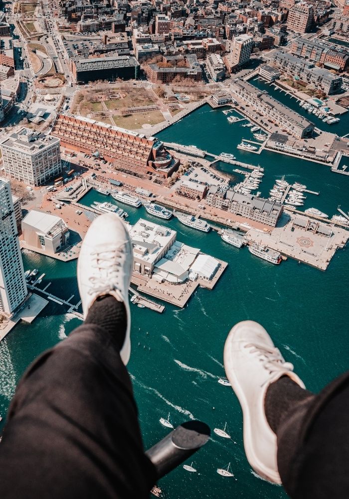 a person dangles their feet from a helicopter flying over the Boston skyline