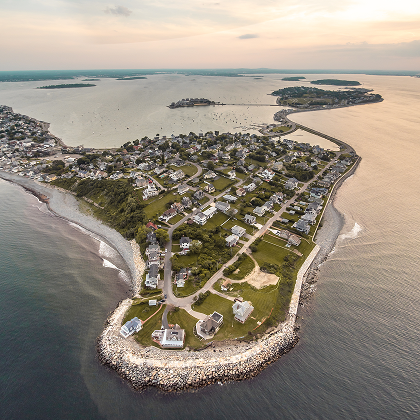 Aerial view of a Boston-area coastal neighborhood surrounded by harbor water at sunset.