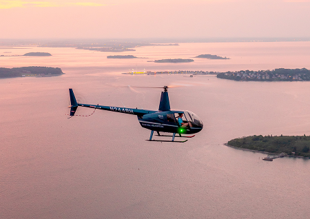 Helicopter flying over Boston Harbor at sunset with islands and water views in the background.