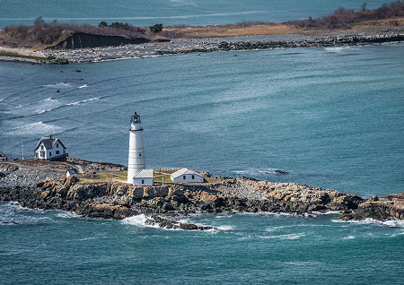 Aerial view of Boston Light on a rocky island surrounded by blue ocean water.